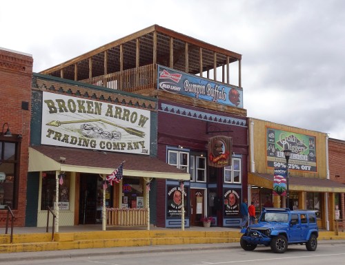 A street view of a trading company with a blue jeep parked outside and a wooden balcony above.