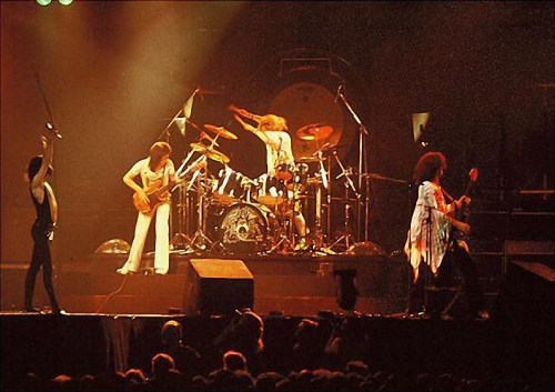 A rock band performs on stage with dramatic lighting, featuring a guitarist, drummer, and vocalist in dynamic poses.