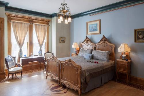 Elegant bedroom featuring a vintage bed, ornate furniture, and large windows with sheer curtains. Soft lighting enhances the ambiance.