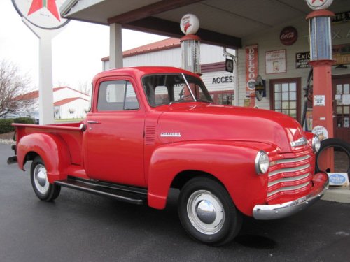 A vintage red Chevrolet pickup truck parked in front of a retro gas station.