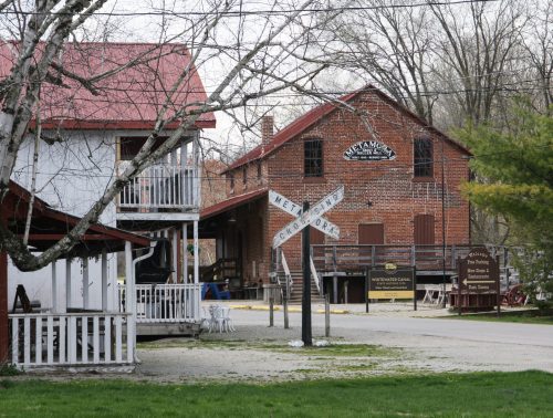 Historic buildings with a red roof, wooden balconies, and a railroad crossing sign in a rural setting.