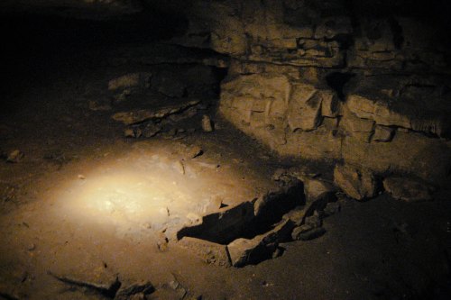Dimly lit cave interior with rocky walls and a small illuminated area on the ground.