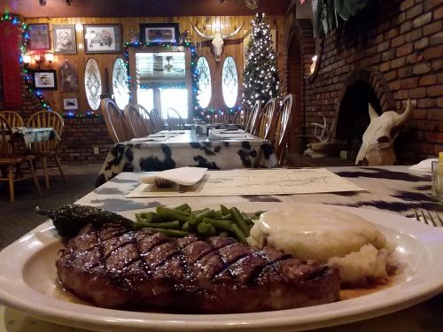 A plate of steak, green beans, and mashed potatoes in a rustic restaurant decorated for the holidays.