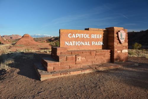 Sign for Capitol Reef National Park with red rock formations and distant snow-capped mountains in the background.