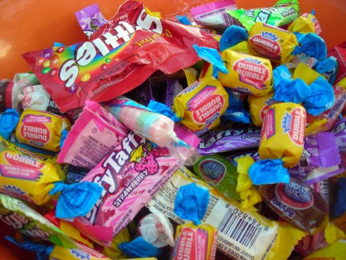 A colorful assortment of various candies, including wrappers in bright pink, yellow, blue, and red, in a bowl.
