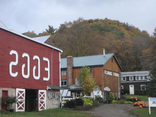 A red barn with "2003" painted on it, alongside a wooden farm building and autumn foliage in the background.