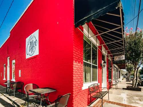 A vibrant red coffee shop exterior with outdoor seating and a sign, set against a clear blue sky.