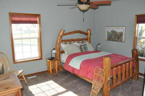 Cozy bedroom with a log bed, colorful bedding, and large windows letting in natural light.