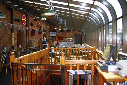 Interior of a restaurant with a glass roof, wooden railings, and tables. A few patrons are seated, and staff are present.