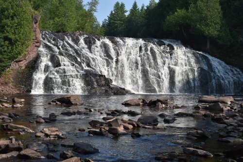 A serene waterfall cascades over rocky cliffs, surrounded by lush green trees and reflecting in a calm pool below.