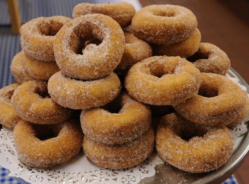 A stack of golden-brown, sugar-coated donuts arranged on a decorative plate.