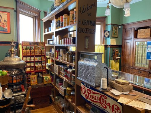 A vintage grocery store interior with shelves of canned goods, a cash register, and retro signage.