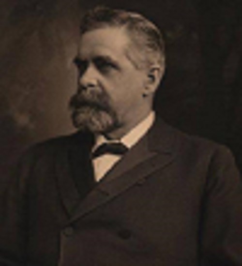 A sepia-toned portrait of a man with a mustache, wearing a suit and bow tie, looking thoughtfully to the side.
