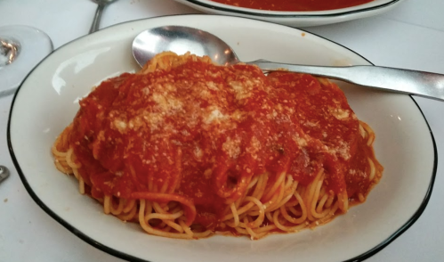 A plate of spaghetti topped with marinara sauce and grated cheese, served with a spoon on a white tablecloth.