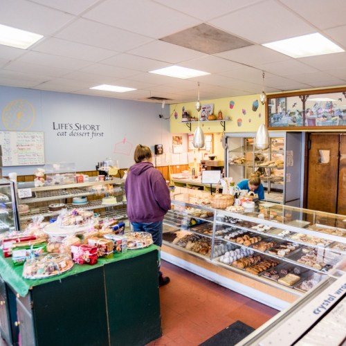 A cozy bakery interior with a display of desserts and pastries, featuring a customer and a staff member behind the counter.