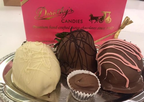 A silver platter with three decorative chocolates and a small chocolate cup, set against a pink box of Dorothy's Candies.