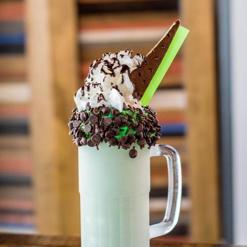 A tall glass filled with mint green milkshake, topped with whipped cream, chocolate chips, and a cookie.