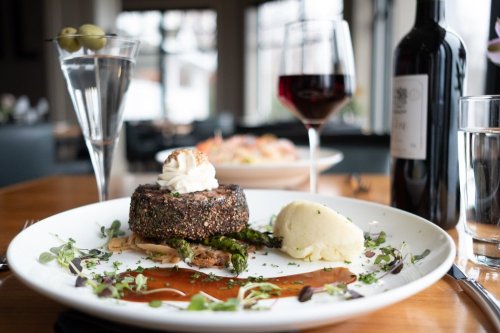 A gourmet meal featuring a beef filet, mashed potatoes, asparagus, and sauces, accompanied by wine and cocktails.