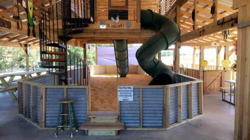 Indoor play area featuring a spiral staircase, a slide, and a sand-filled play zone with seating.