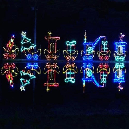 Colorful holiday lights shaped like trains and festive symbols, reflecting on water at night.