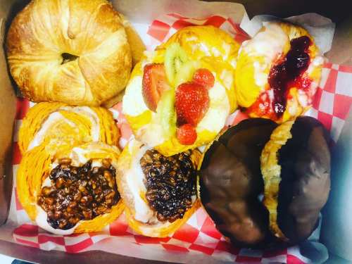 A box of assorted pastries, including croissants and sweet rolls topped with fruit and icing, on a red checkered liner.