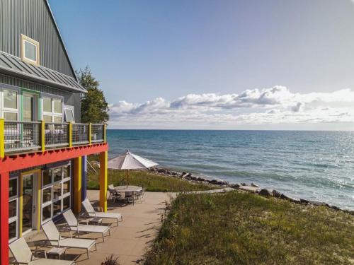 A colorful building by the shore with lounge chairs and an umbrella, overlooking a calm lake and cloudy sky.