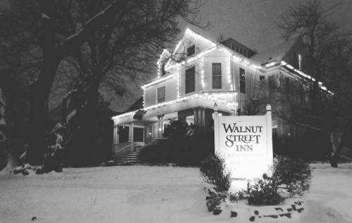 A snow-covered Walnut Street Inn, adorned with festive lights, stands peacefully at night.