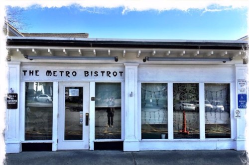 Exterior of The Metro Bistrot, featuring large windows and a white facade, with a clear blue sky above.