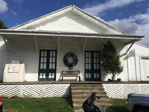 A white building with green doors, a wreath on the front, and a bench on the porch, surrounded by a blue sky.