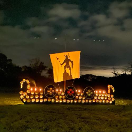 A lit display of a Viking ship with a flag featuring a horned figure, set against a night sky with clouds.