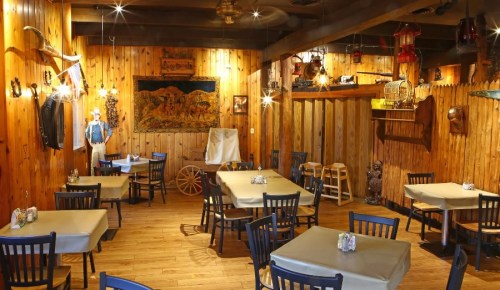 Cozy restaurant interior with wooden walls, tables set for dining, and rustic decor including lanterns and wall art.