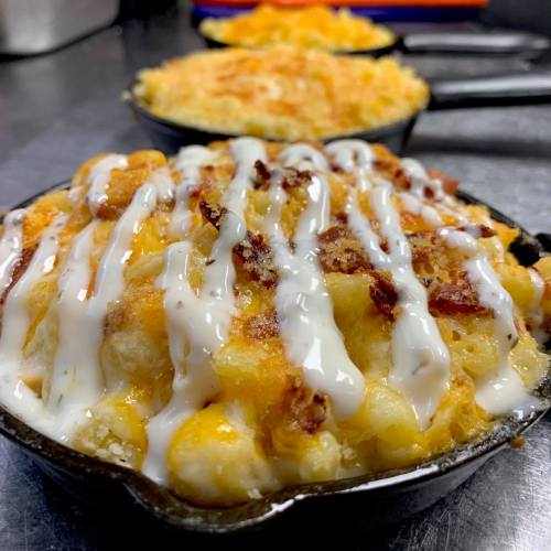 Close-up of creamy mac and cheese topped with crispy bacon and drizzled with sauce, served in a cast iron skillet.
