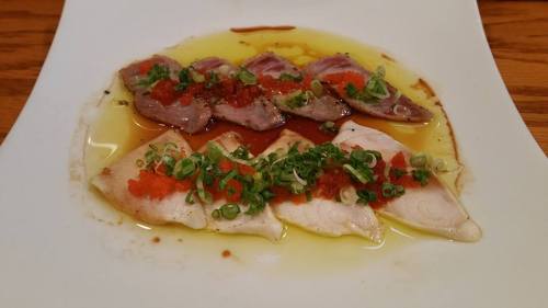 Sliced fish drizzled with oil, topped with green onions and red roe, served on a white plate.