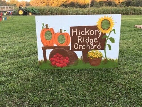 A colorful sign for Hickory Ridge Orchard featuring pumpkins, apples, and a sunflower in a grassy field.