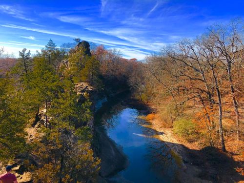 A scenic view of a river winding through autumn trees under a blue sky with wispy clouds.