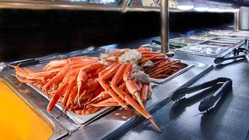 A large pile of cooked crab legs on a buffet table, with various condiments and utensils in the background.