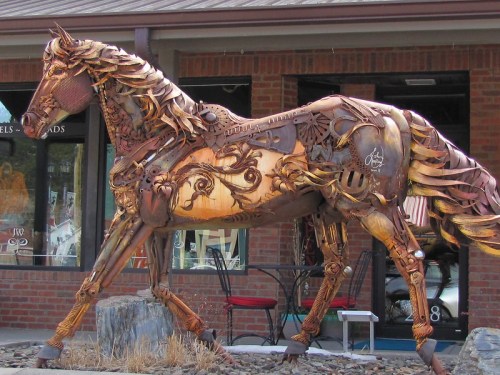 A large, artistic horse sculpture made from metal and various materials, displayed outside a brick building.