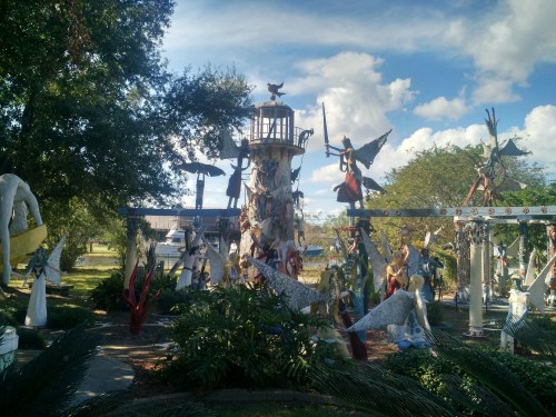 A whimsical outdoor sculpture garden featuring various angelic figures and a lighthouse surrounded by greenery.
