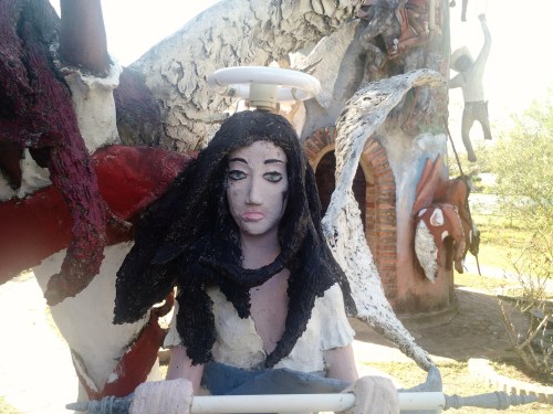A sculptural figure with dark hair and a serene expression, surrounded by abstract, colorful forms and figures.