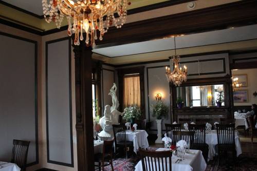 Elegant dining room with chandeliers, white tablecloths, and a statue, featuring classic decor and floral arrangements.