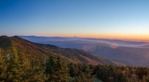 A panoramic view of mountains at sunset, with layers of hills and a colorful sky in the background.