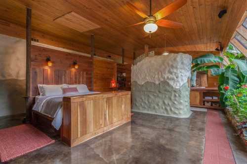 Cozy bedroom with wooden decor, a unique curved wall, and large windows surrounded by greenery.
