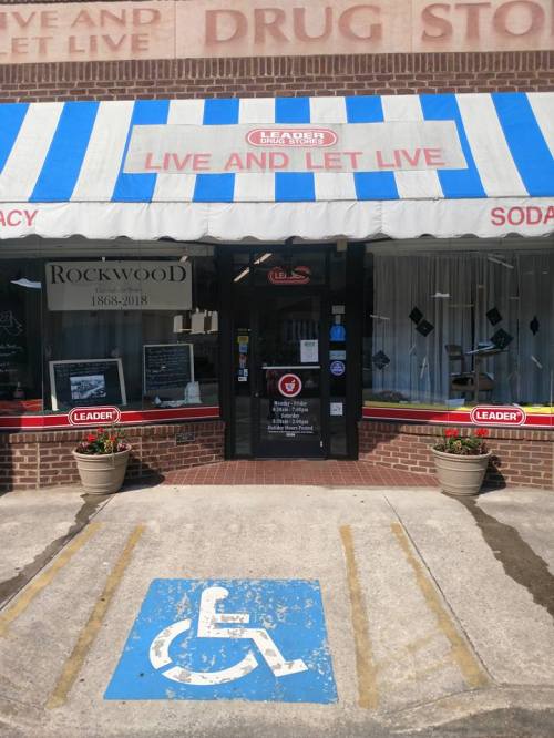 Entrance of a drug store with a blue and white striped awning, featuring a wheelchair accessibility symbol on the pavement.
