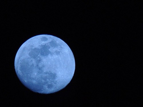 A close-up view of a bright blue moon against a dark night sky.