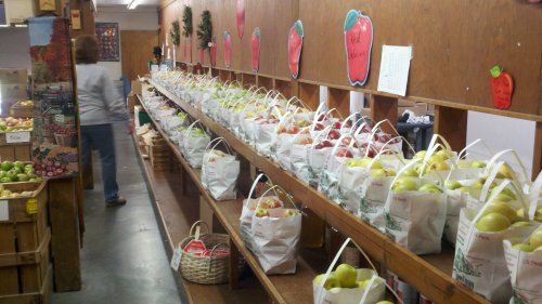 A market interior with shelves lined with bags of apples and a person walking in the background.