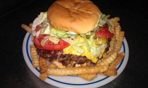 A juicy cheeseburger topped with lettuce, tomato, and mustard, served with a side of crinkle-cut fries on a plate.