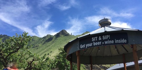 A gazebo with a sign reading "Sit & Sip! Get your beer & wine inside" against a backdrop of green mountains and blue sky.