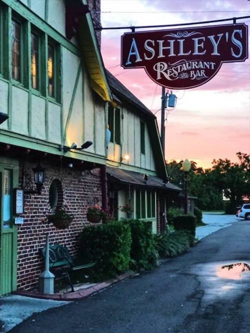 A charming restaurant with a sign reading "Ashley's Restaurant Bar," set against a colorful sunset.