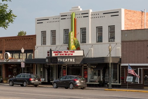 Historic theater building with a marquee advertising a film tour, surrounded by parked cars and an American flag.