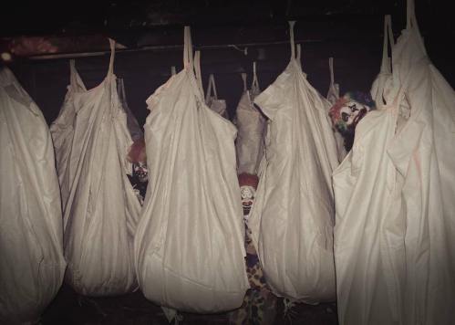 Creepy scene with clowns partially hidden in white bags, creating an eerie and unsettling atmosphere.